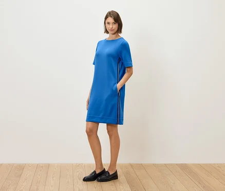 Eine Frau steht und posiert in einem blauen, kurzärmeligen Kleid und schwarzen Loafers.