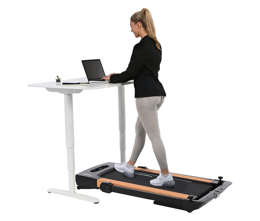 Frau geht auf einem Laufband 2 in 1 in Holzoptik und tippt auf einem Laptop, der auf einem höhenverstellbaren Schreibtisch steht.