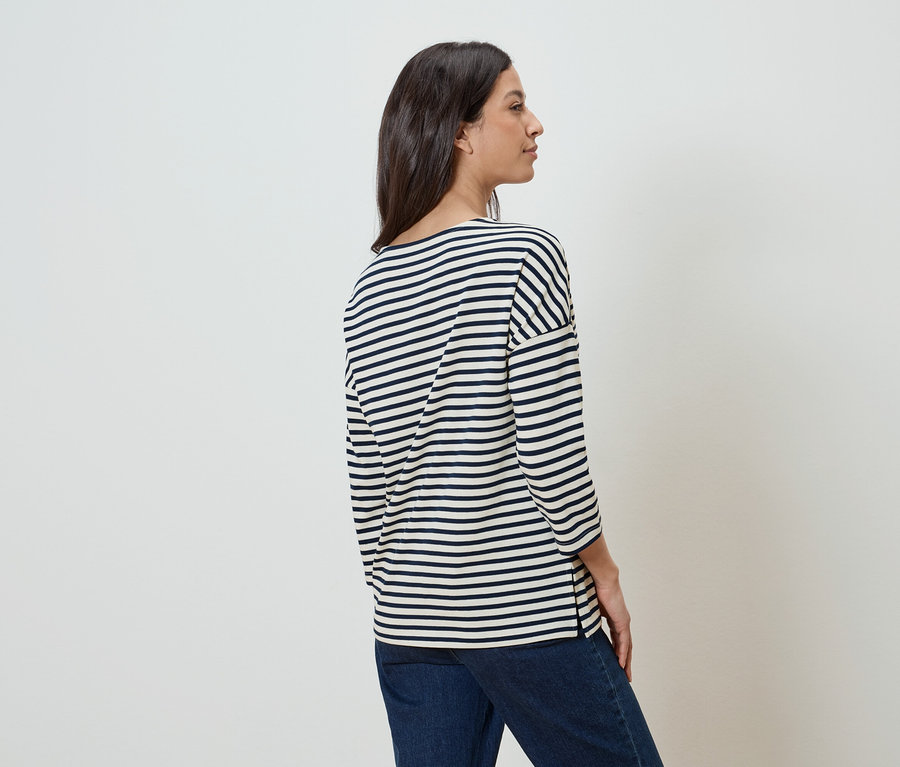 Eine Frau steht seitlich und trägt ein gestreiftes Oberteil und Jeans.