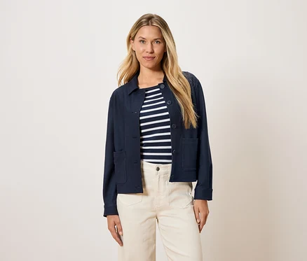 Frau trägt eine marineblaue Jacke über einem gestreiften Oberteil und cremefarbene Hosen.