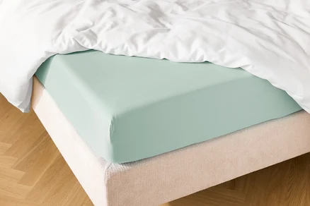 Nahaufnahme eines Bettes mit hellblauem Spannbettlaken und einer weißen Bettdecke.