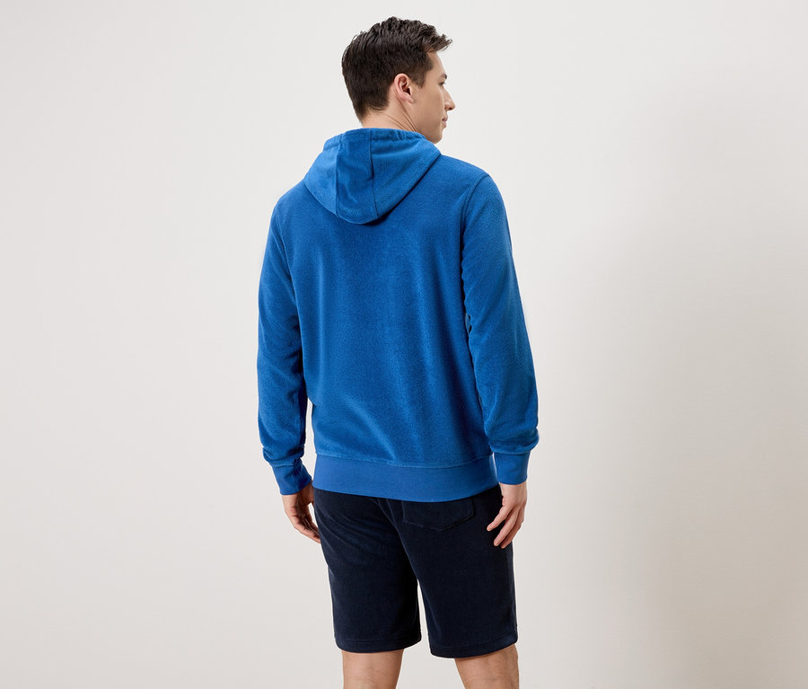 Mann von hinten in blauem Frottee-Hoodie und Shorts vor einem neutralen Hintergrund.