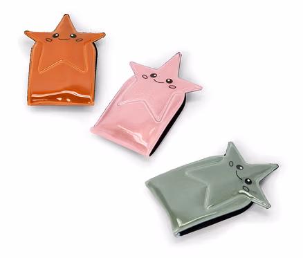 Drei glänzende, sternförmige Etuis in Orange, Rosa und Salbeigrün, jedes mit einem lächelnden Cartoon-Gesicht, diagonal auf weißem Hintergrund angeordnet.