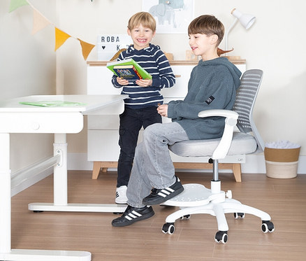 Zwei Jungen an einem weißen Roba Kinderschreibtisch mit Kinderbürostuhl Set. Einer sitzt, der andere steht mit Buch.