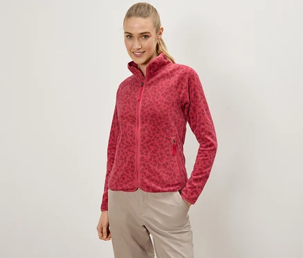 Frau mit einer roten Fleecejacke mit Blumenmuster und beigen Hosen, die mit einer Hand in der Tasche posiert.