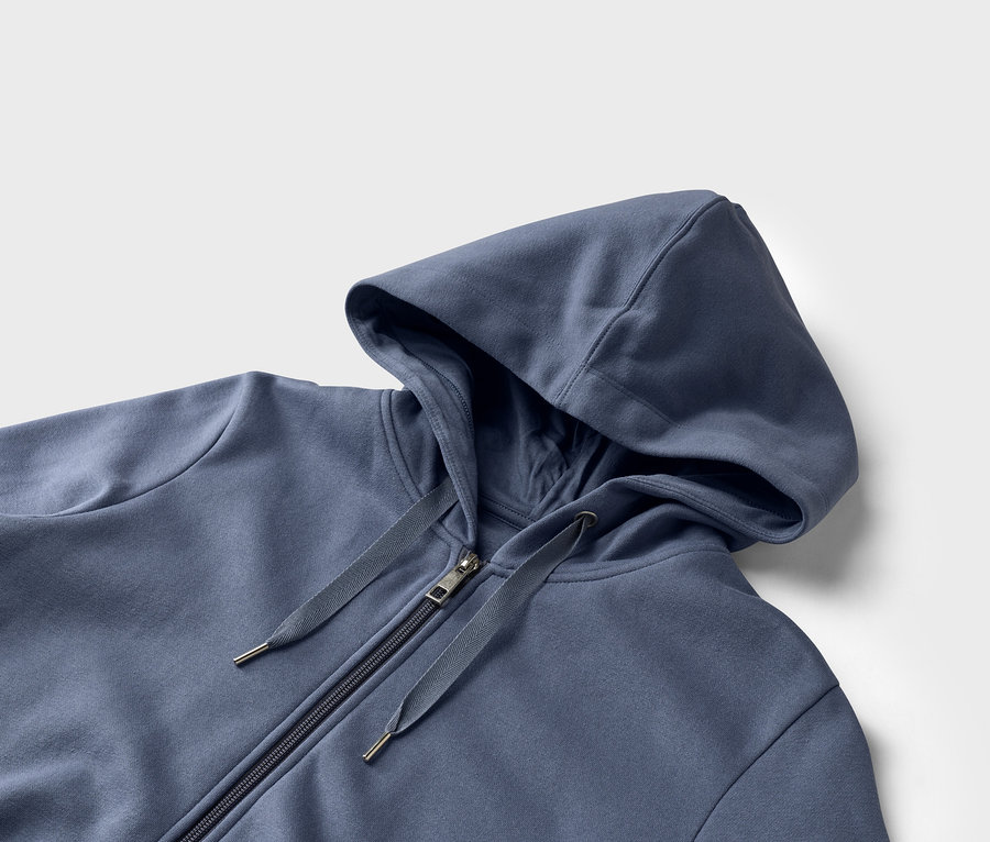 Nahaufnahme eines blauen Kapuzenpullovers mit Reißverschluss vor einem weißen Hintergrund.