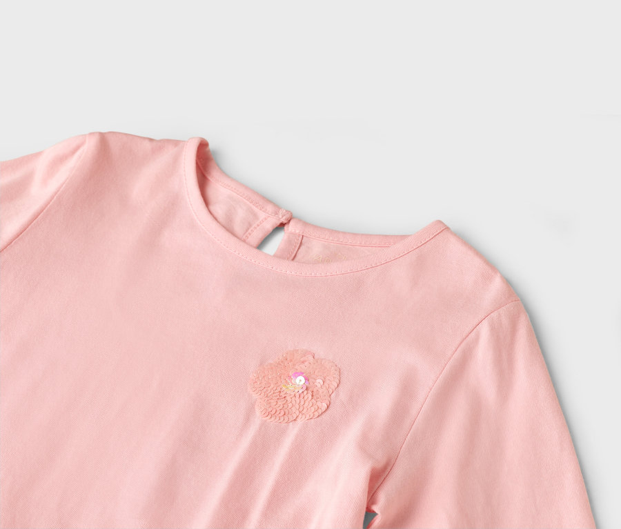 Nahaufnahme eines rosafarbenen Kleides mit einer Paillettenblume auf der Brust.