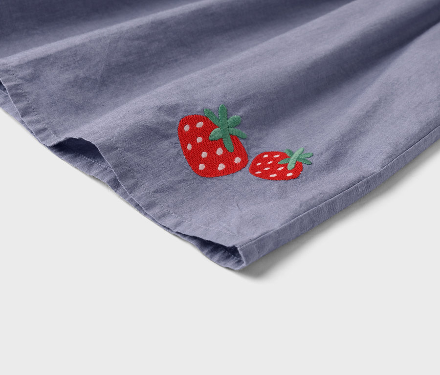 Detailansicht eines lilafarbenen Stoffes mit zwei aufgestickten Erdbeeren.