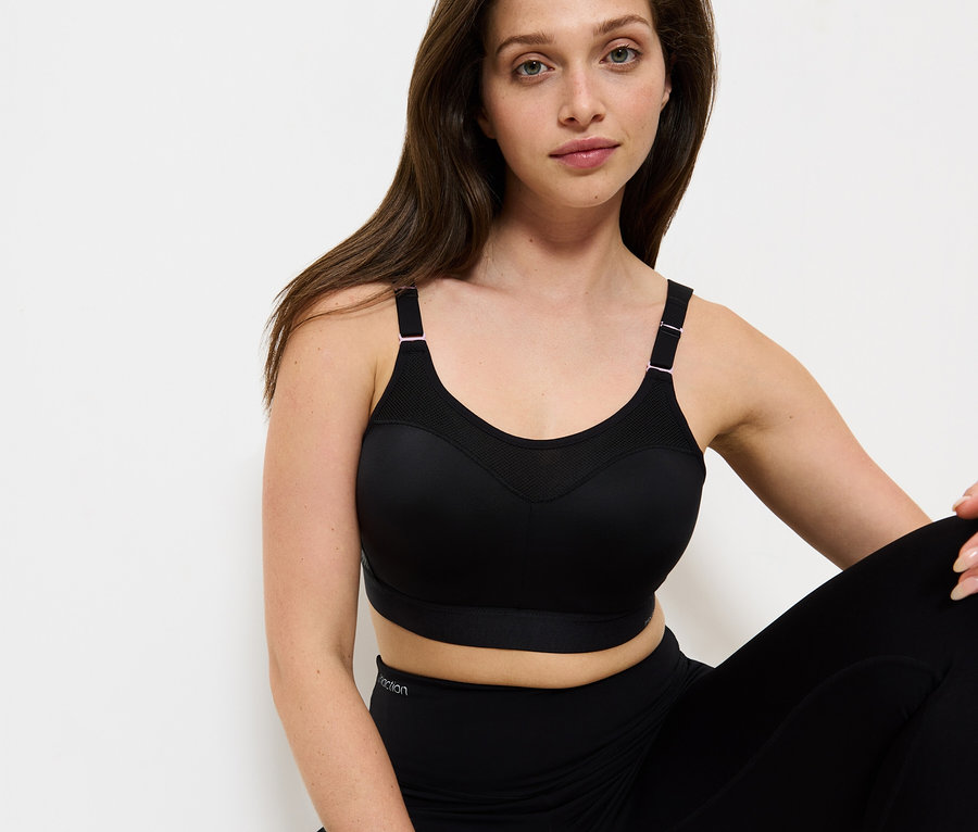 Frau sitzt und trägt einen schwarzen Sport-BH und Leggings.