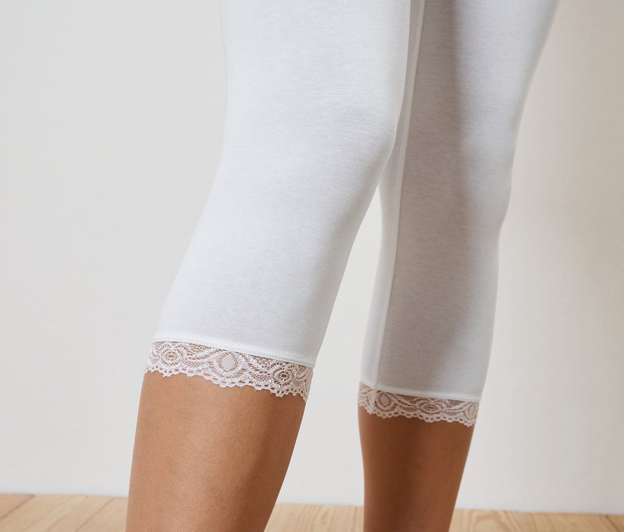 Nahaufnahme von Beinen in weißen, knielangen Leggings mit Spitzensaum.