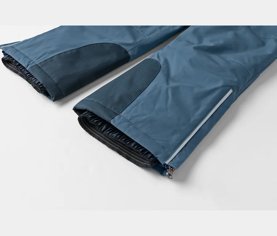 Zwei blaue Outdoor-Hosenbeine mit dunkleren blauen Patches, elastischen Innenbündchen und äußeren Reißverschlüssen mit reflektierenden Streifen.
