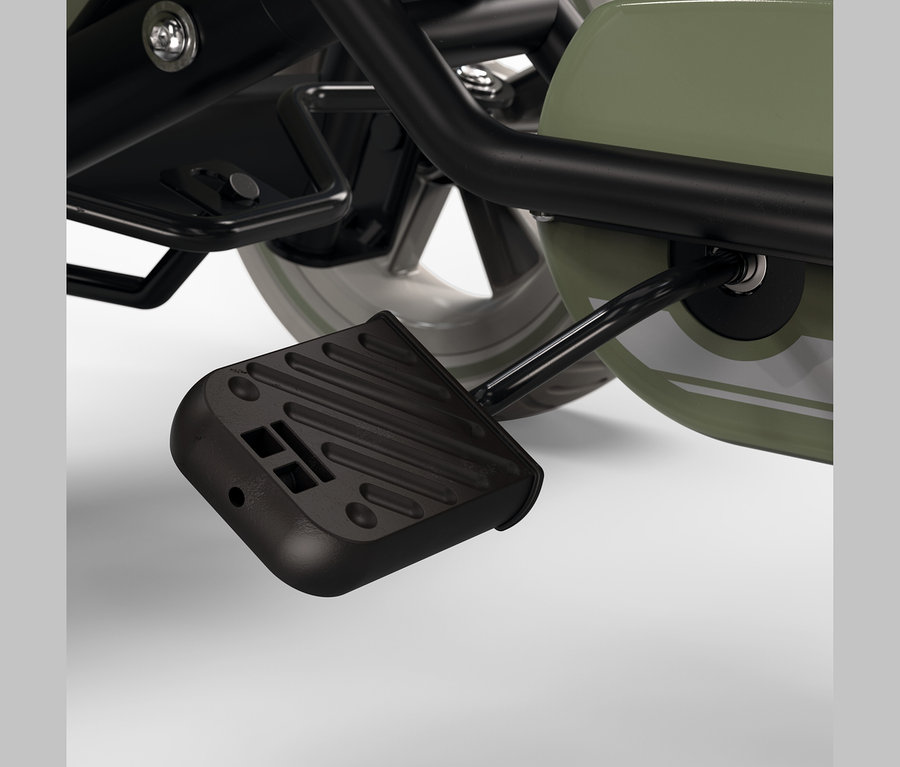 Nahaufnahme eines schwarzen Fußpedals an einem Kinderfahrzeug, verbunden mit einem olivgrünen Radgehäuse, mit teilweise sichtbarem silbernem Rad und schwarzem Rahmen.