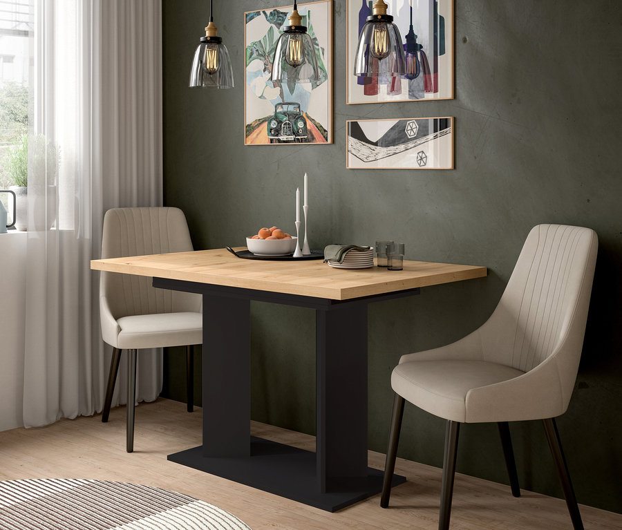 Esszimmer mit hellem Holztisch, schwarzem Untergestell und zwei beigefarbenen Polsterstühlen. Auf dem Tisch stehen Obst, Kerzen, Teller und Gläser. Drei Pendelleuchten hängen darüber, gerahmte Kunstwerke schmücken die dunkle Wand.