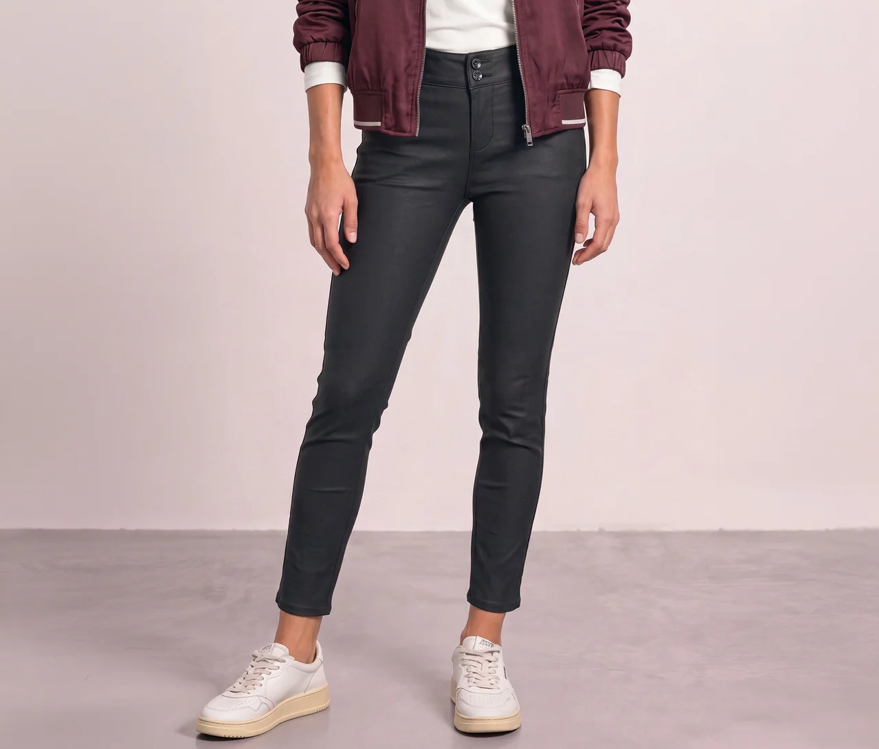 Eine Person trägt eine schwarze Street One Hose in Lederoptik, ein weißes Oberteil, eine bordeauxrote Jacke und weiße Sneaker.