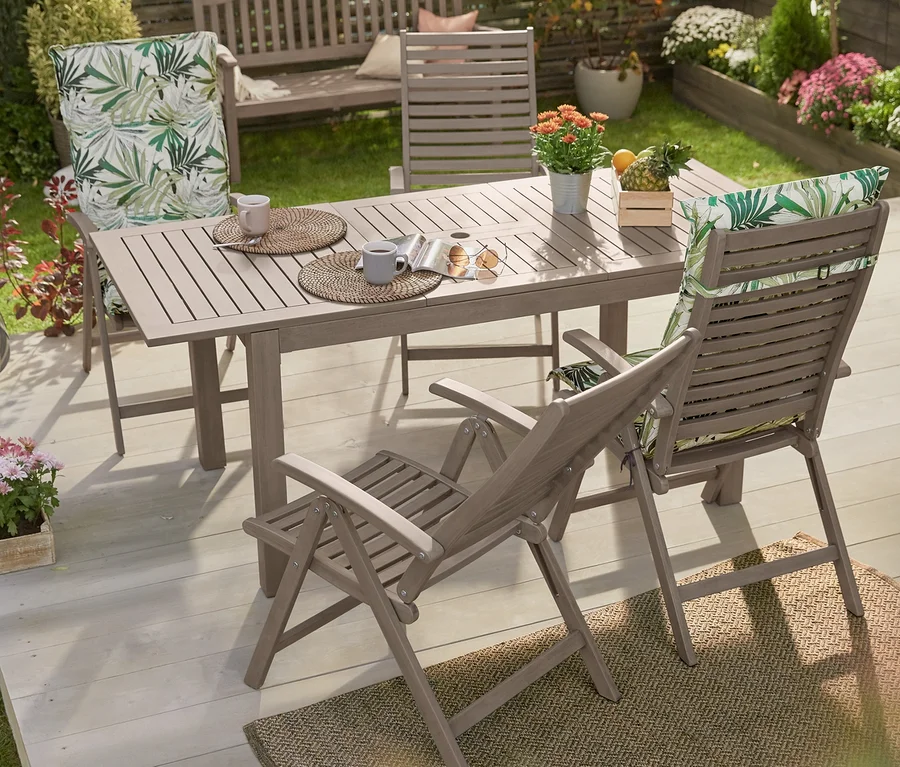 Ein Ausziehbarer Gartentisch, vintage grey, umgeben von Hochlehnern mit Print-Auflage und einer Gartenbank, Vintage Grey, auf einer Holzterrasse.