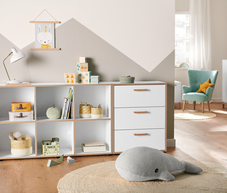 Zimmer mit Kommode mit Furnierkante, 2 Aufbewahrungskörben und Riesen-Plüschwal auf rundem Teppich.