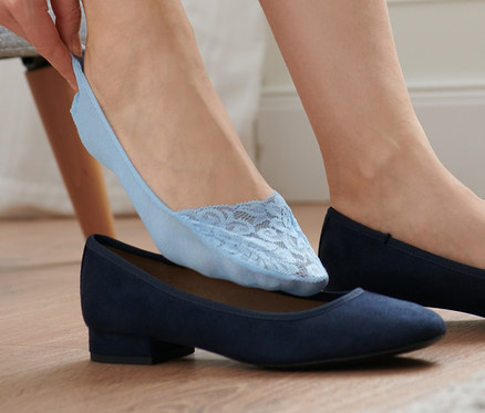 Frau zieht blaue Ballerina-Füßlinge mit Spitze auf ihren Fuß, der in einem blauen Ballerina-Schuh steckt.