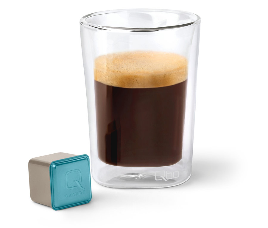 Qbo Caffè Grande KIRINYAGA BAYA Kapsel neben einem Glas Kaffee.