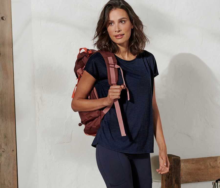 Frau mit braunem Rucksack posiert in blauem Sportshirt.