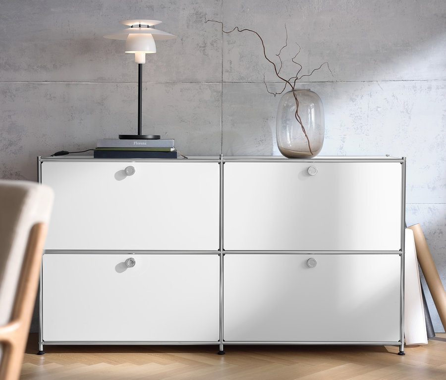 Weißes Sideboard »CN3« mit vier Klappen, darauf eine Tischleuchte aus Metall und eine Vase mit Zweigen.