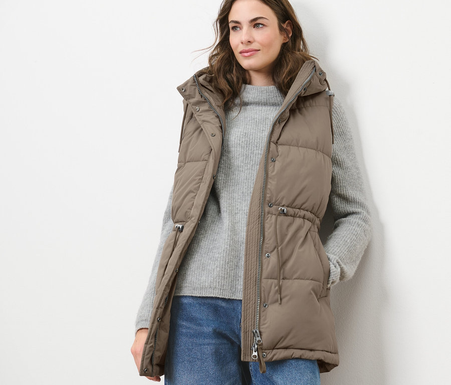 Frau trägt eine Stepp-Weste mit Kapuze, einen Pullover und Jeans.