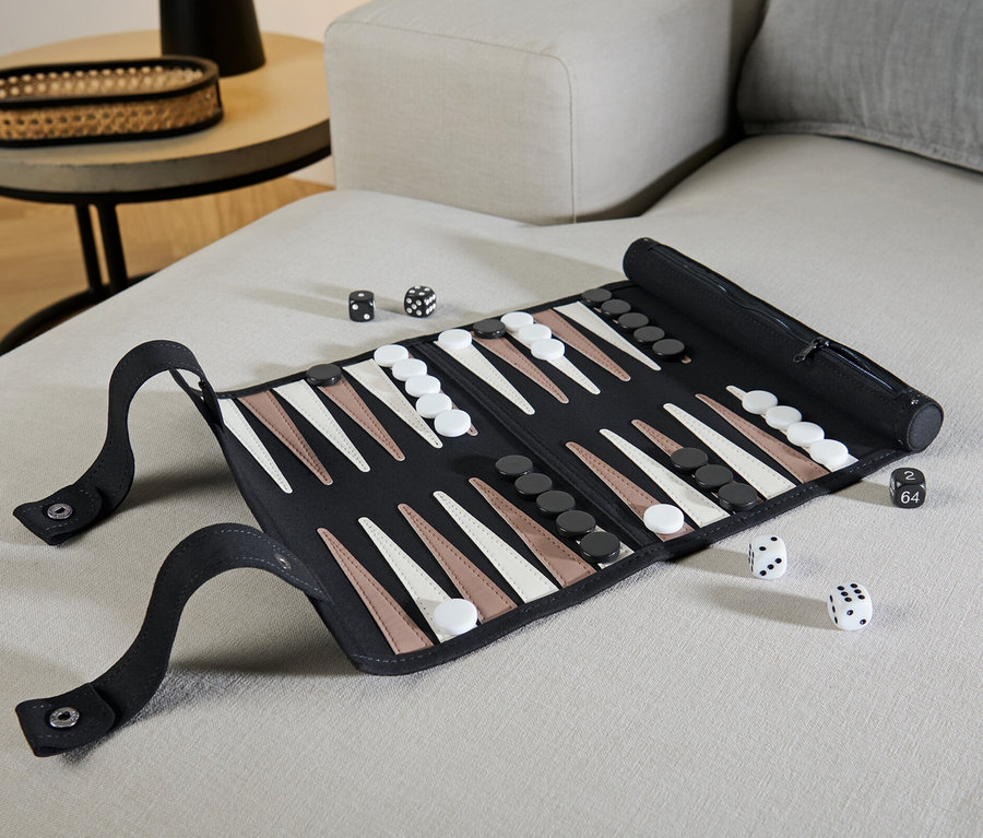 Auf einem beigen Sofa liegt ein aufgerolltes Backgammon-Spiel mit Würfeln.
