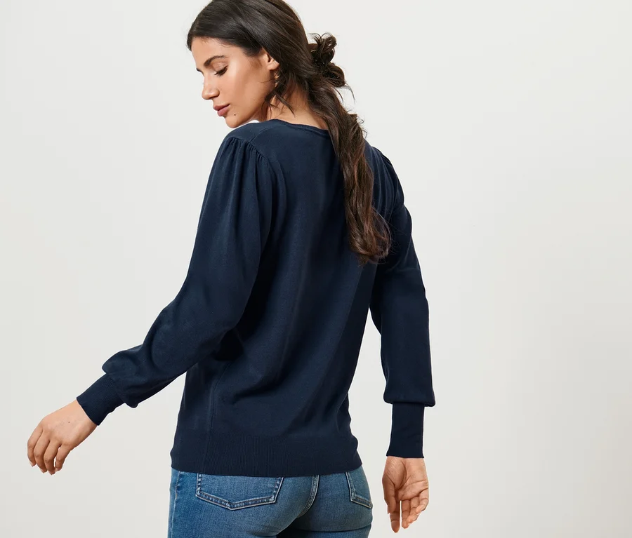 Frau posiert in Feinstrickpullover und Jeans.