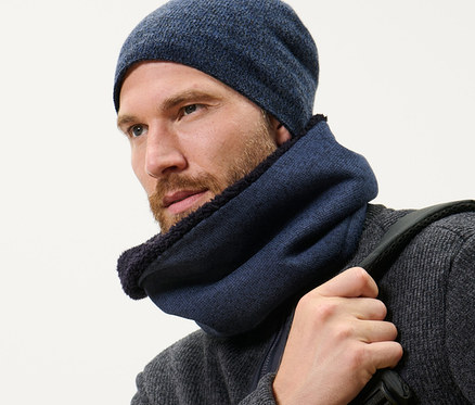 Mann mit Bart trägt einen dunkelblauen Strickfleece-Schlauchschal und eine Mütze und trägt einen Rucksack.