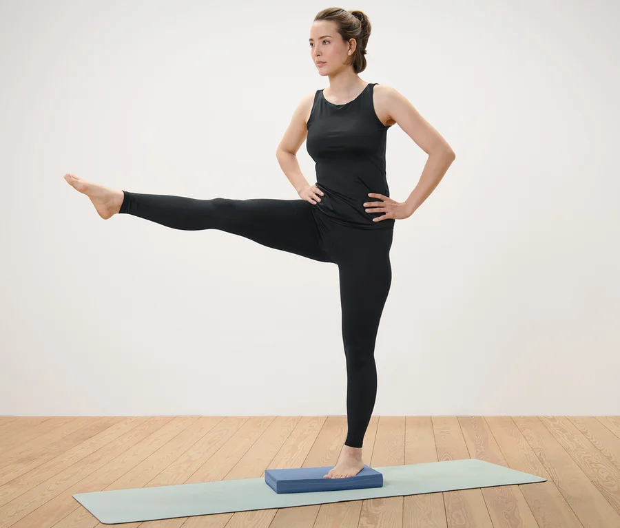 Frau steht auf Balance Pad und hebt ein Bein.