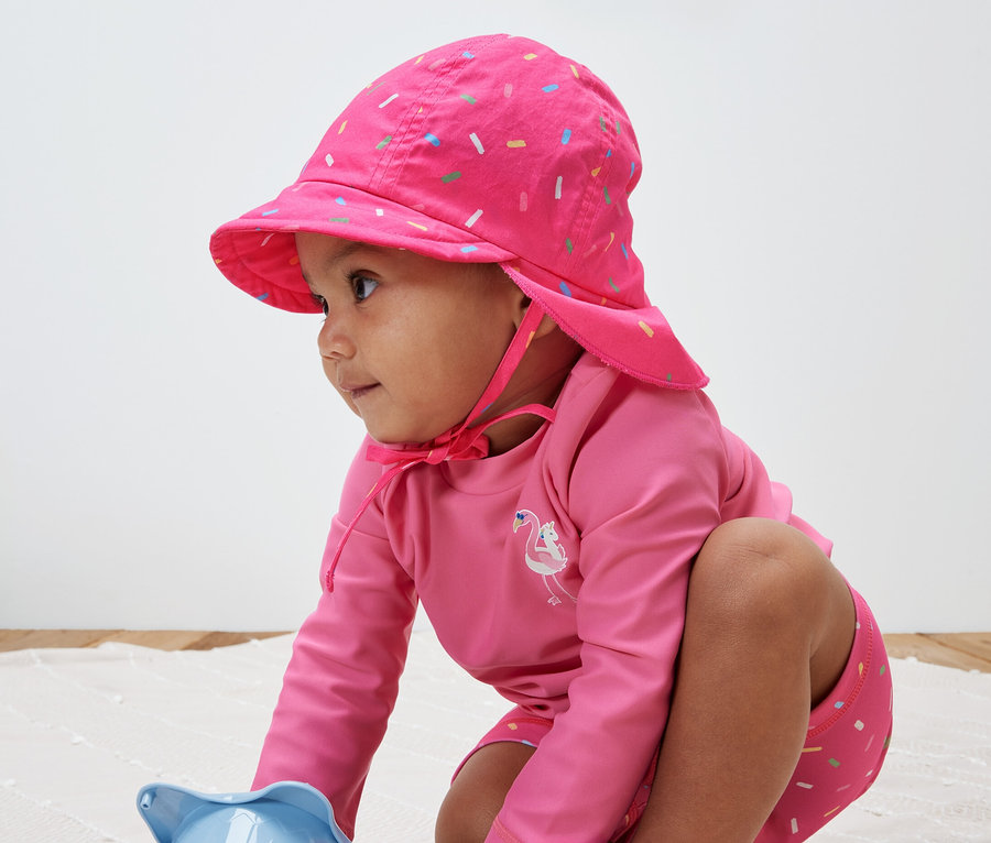 Kind spielt mit Spielzeug und trägt eine pinke Kinder-Sonnenmütze mit UV-Schutzfaktor 80.