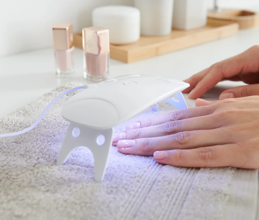 Frau trocknet Nägel unter LED-UV-Nageltrockner.
