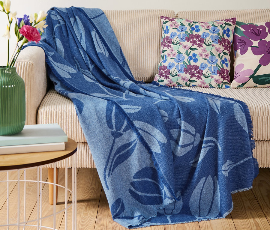 Auf einem beigen Sofa liegt eine blaue Wohndecke mit Fransen.