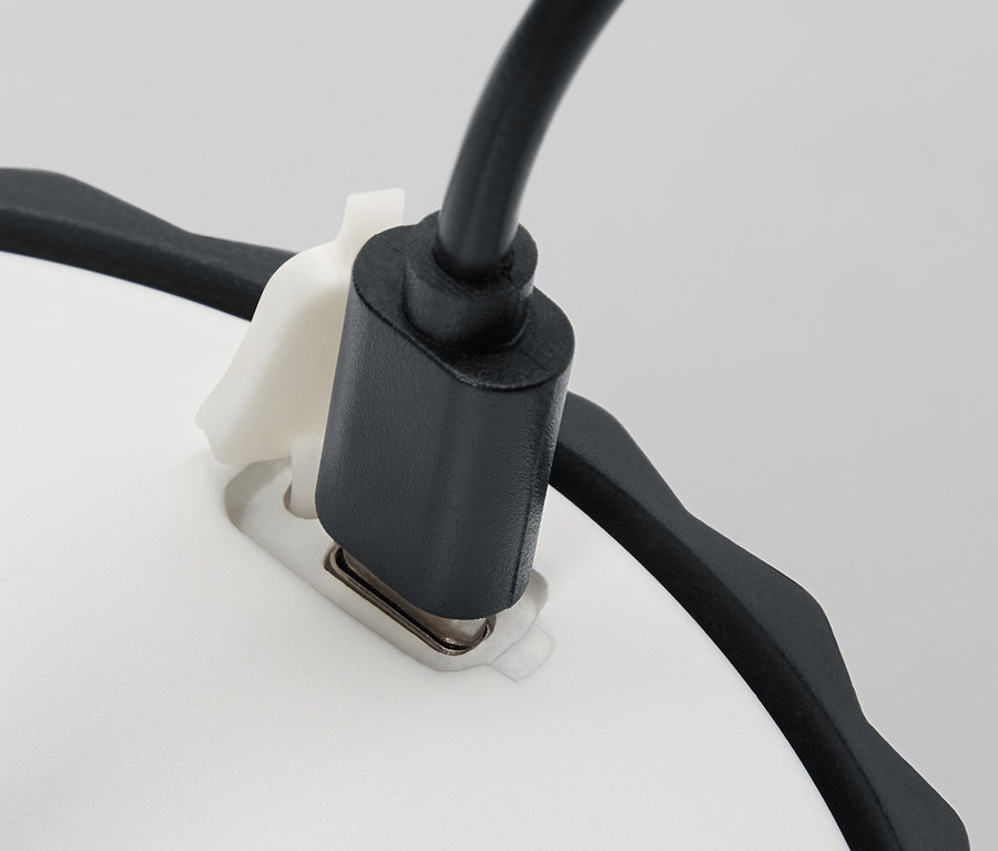 Detailansicht einer kleinen LED-Tischleuchte mit einem schwarzen Stromkabel, das in die weiße Basis eingesteckt ist.