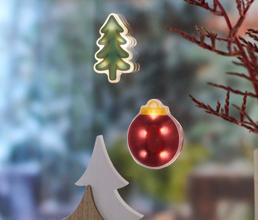 LED-Fensterbilder in Form eines Baumes und einer Kugel sind am Fenster angebracht. Neben dem Fenster steht eine Vase mit einer Pflanze.