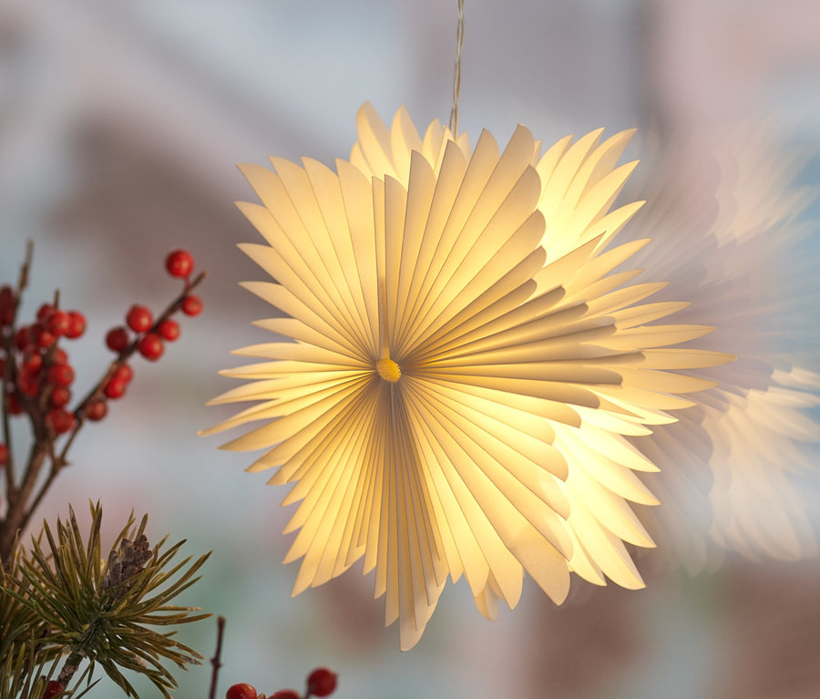 Ein kleiner LED-Papierstern hängt an einem Fenster, neben Zweigen mit roten Beeren.