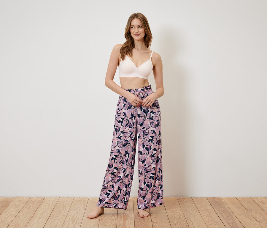 Eine Frau steht und trägt einen BH und eine weite Hose mit Blumenmuster.
