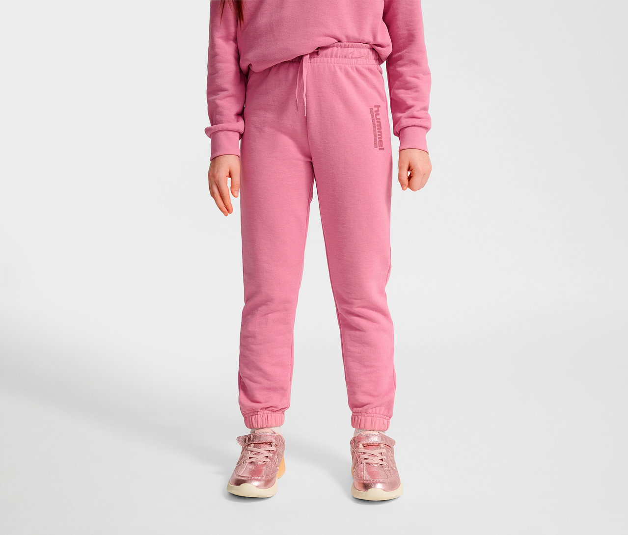 Mädchen trägt rosa HUMMEL HMLJR Base Regular Pants und rosa Schuhe.