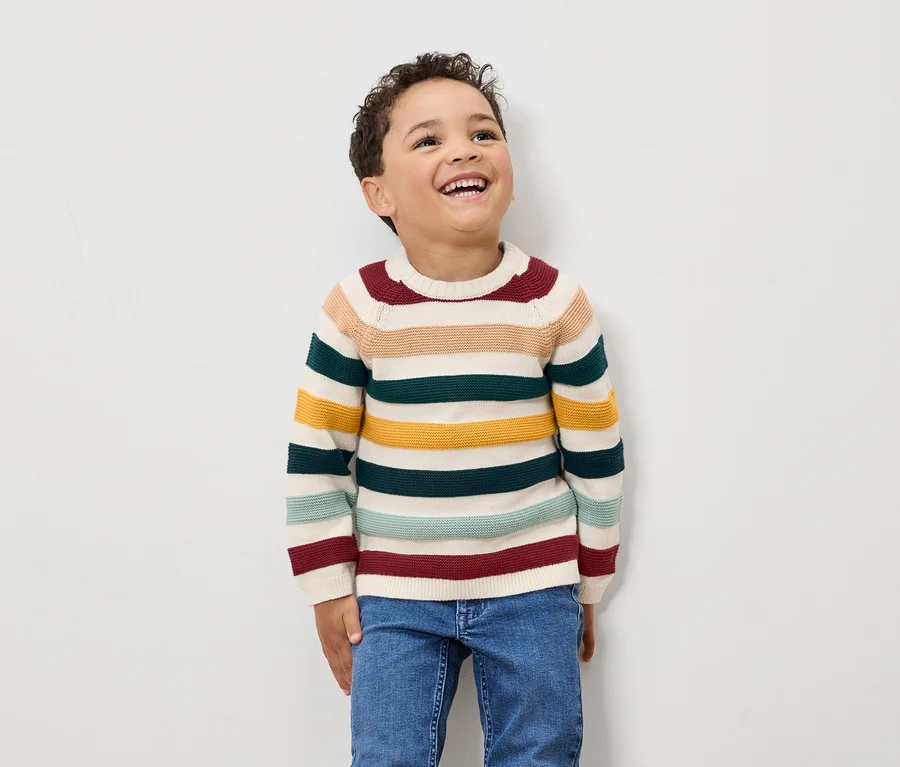 Ein Junge lacht und trägt einen gestreiften Pullover und Jeans.