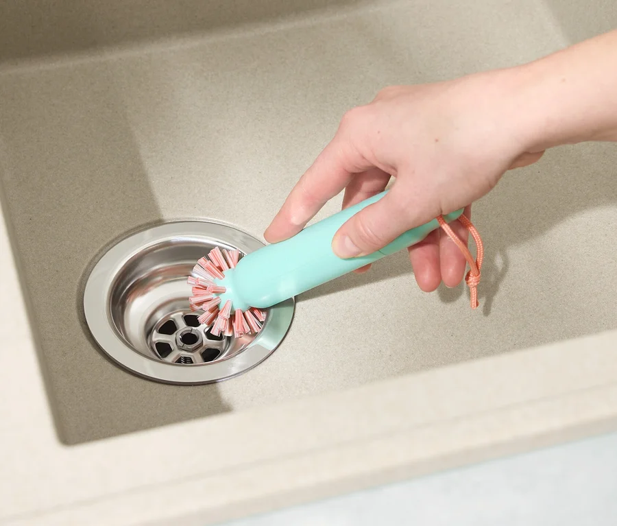 Eine Hand reinigt einen Abfluss im Waschbecken mit einer 2-in-1-Abflussbürste.