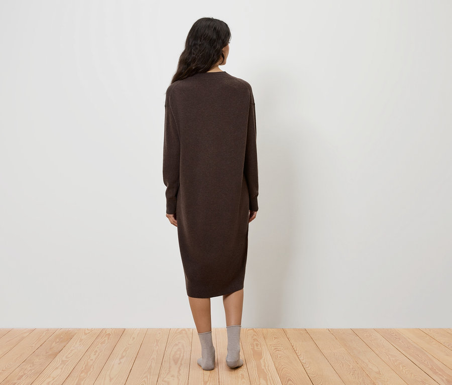 Eine Frau steht mit dem Rücken zur Kamera und trägt ein braunes Kleid und graue Socken.
