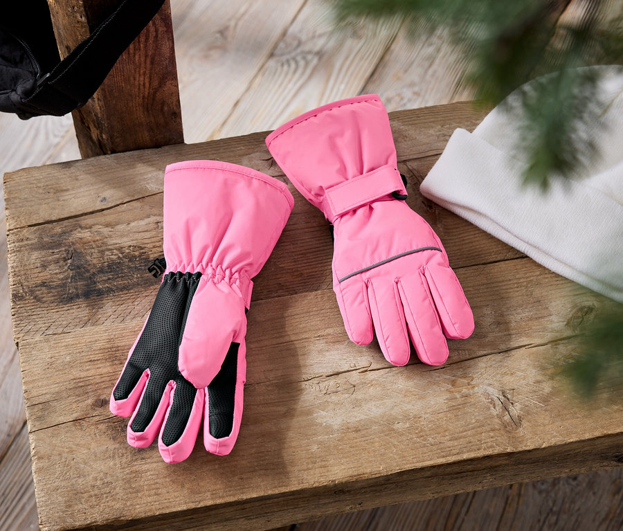 Auf einer Holzbank liegen ein Paar rosa Skihandschuhe und eine weiße Strickmütze. Im Hintergrund ist eine schwarze Mütze zu sehen.