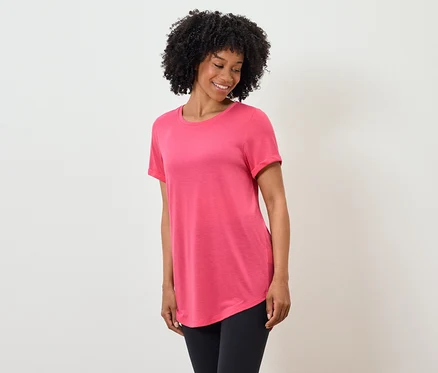 Eine Afroamerikanerin lächelt und trägt ein rosafarbenes T-Shirt und schwarze Leggings.