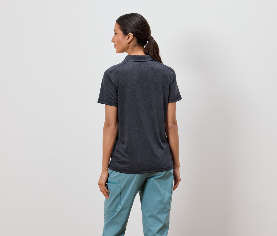 Eine Frau mit Pferdeschwanz steht mit dem Rücken zur Kamera und trägt ein dunkelgraues Poloshirt und hellblaue Hosen.