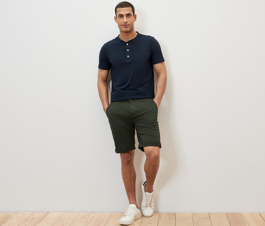 Mann steht mit den Händen in den Hosentaschen. Er trägt ein marineblaues Kurzarm-Henley.