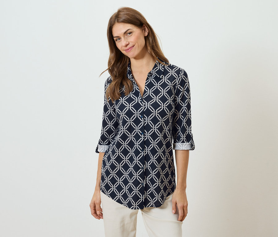 Frau trägt eine marineblaue Bluse mit weißem geometrischen Muster und beigen Hosen.