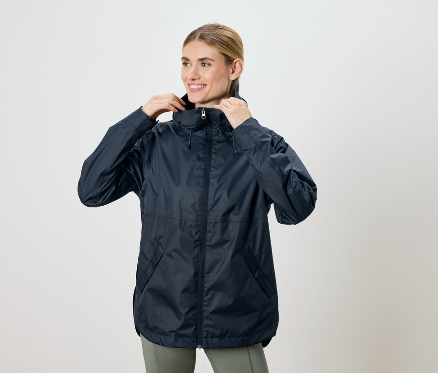 Frau, die eine marineblaue Jacke mit Kapuze anpasst und lächelt.