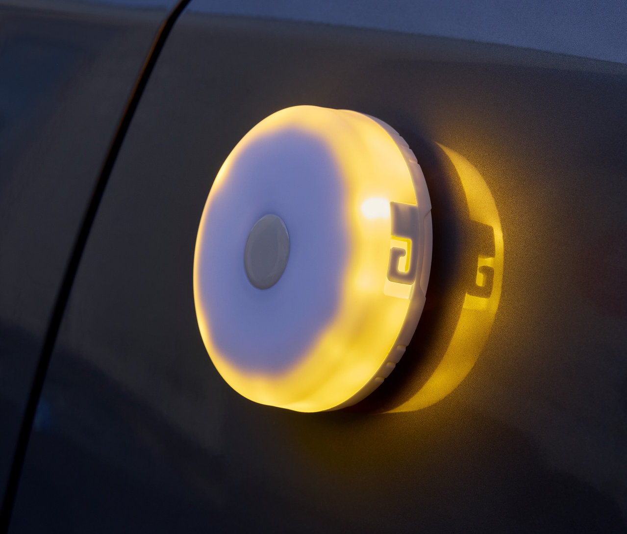 Eine runde, batteriebetriebene Leuchte mit gelbem Licht ist an einer dunklen Oberfläche befestigt.
