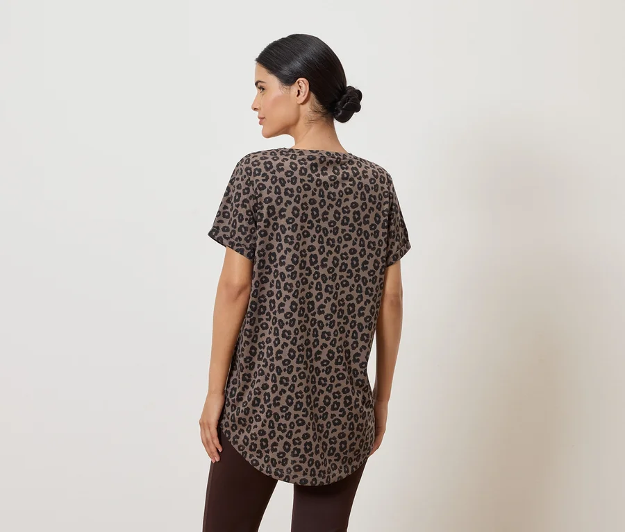 Eine Frau mit Dutt trägt ein braunes, kurzärmeliges Shirt mit schwarzem Leopardenmuster und braune Leggings, von hinten gesehen.