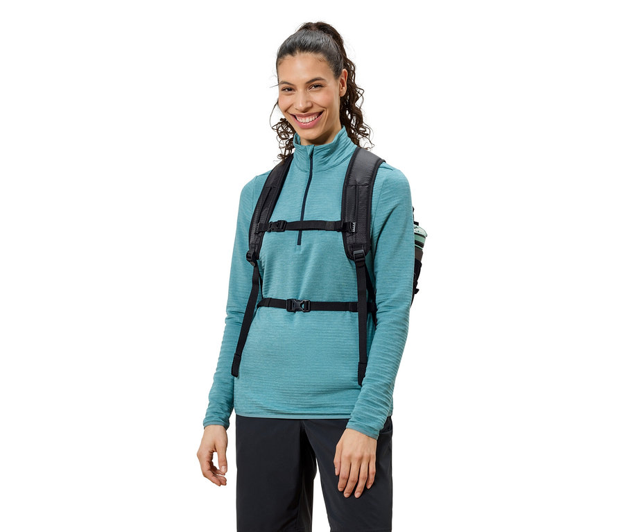 Frau mit schwarzem Rucksack, blauem Oberteil und schwarzen Hosen, lächelnd.