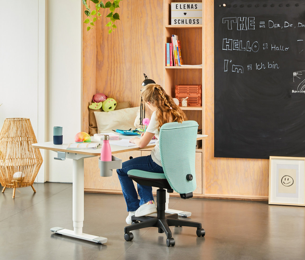 Mädchen sitzt am Schreibtisch auf einem Topstar Sitness »Home S'cool« Bürostuhl in Schwarz und Mintgrün.